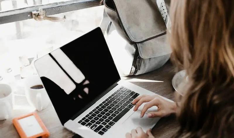girl wearing grey long-sleeved shirt using MacBook Pro on brown wooden table